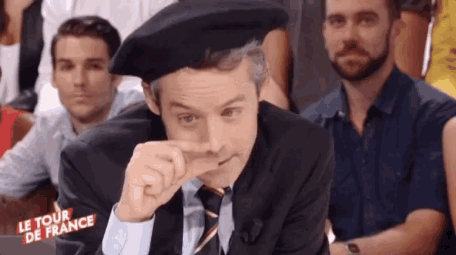 a man in a suit and tie is wearing a beret with the words le tour de france written on it