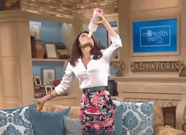 a woman is drinking from a bottle while sitting on a couch in front of a television screen that says meredith vieira