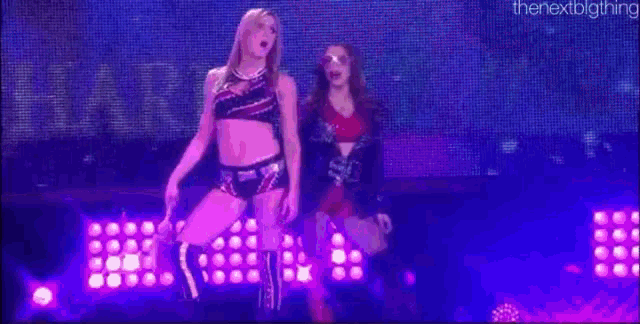 two women are dancing on a stage with purple lights behind them .