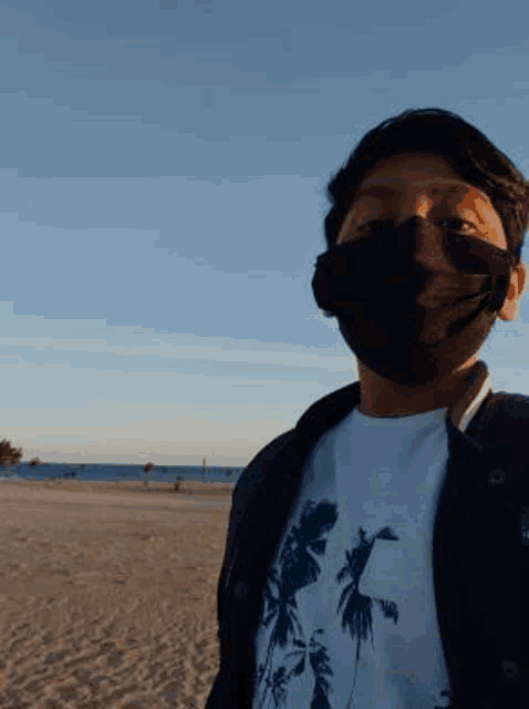 a young man wearing a black face mask is standing on the beach .