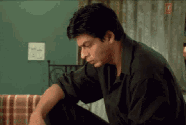 a man in a black shirt is sitting in front of a wall with a light switch