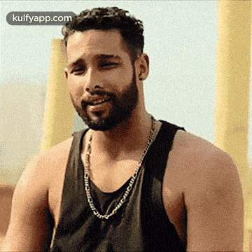 a man with a beard is wearing a black tank top and a gold chain .