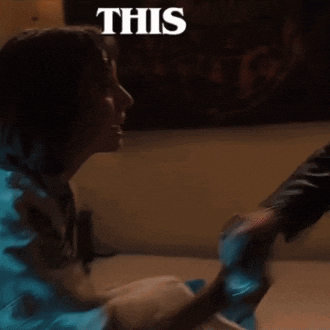 a woman is sitting on the floor with a man holding her hand and a sign that says this .