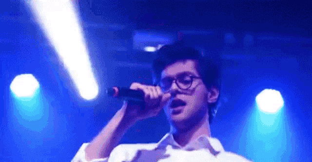 a young man wearing glasses is singing into a microphone on stage .