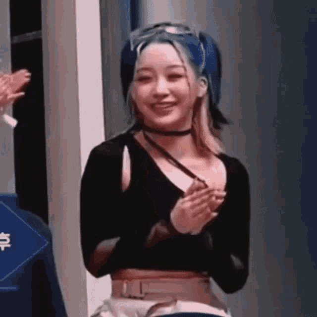 a woman with blue hair is clapping her hands while wearing a choker .