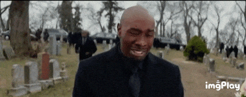 a man in a black suit and tie is crying in a cemetery