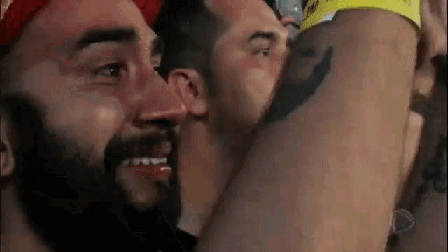 a man with a beard is kissing another man on the cheek in a crowd of people .