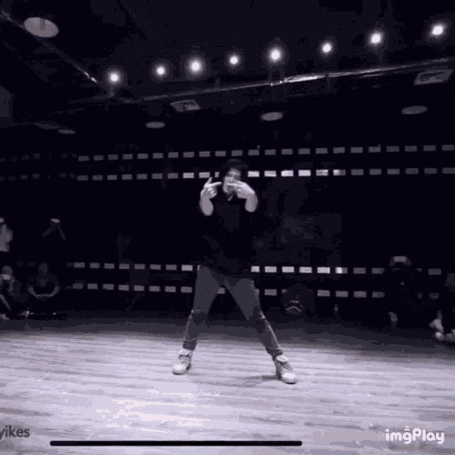 a man in a black shirt is dancing in a dark room while a group of people watch .