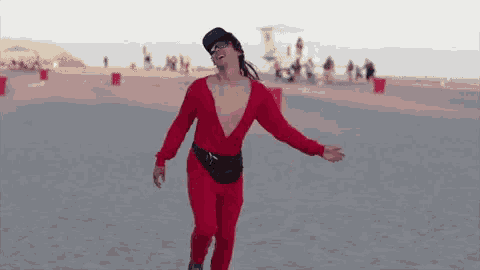 a man in a red jumpsuit and sunglasses is dancing on the beach