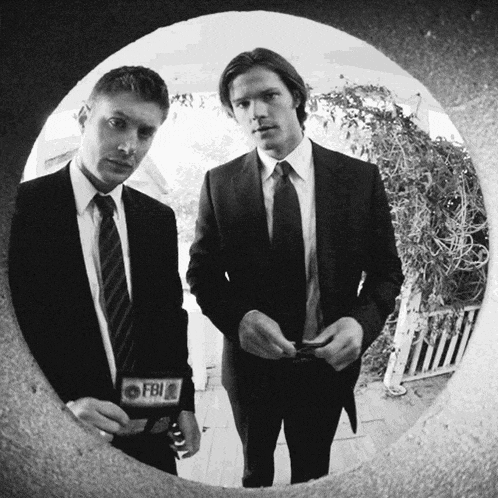 two men in suits and ties are standing next to each other and one has a fbi badge on his jacket