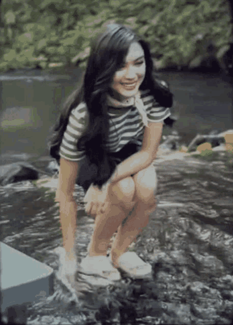 a woman is squatting in the water near a stream .