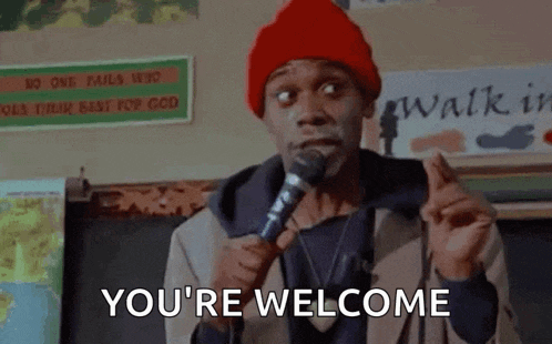 a man in a red hat is holding a microphone and saying `` you 're welcome '' in front of a classroom .