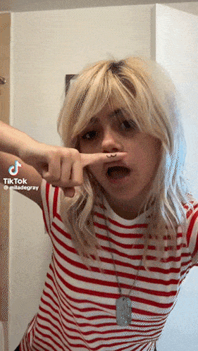 a girl in a red and white striped shirt is making a funny face with her finger in her mouth