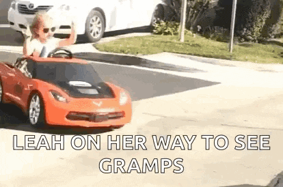 a little girl is driving a red toy car down the street .
