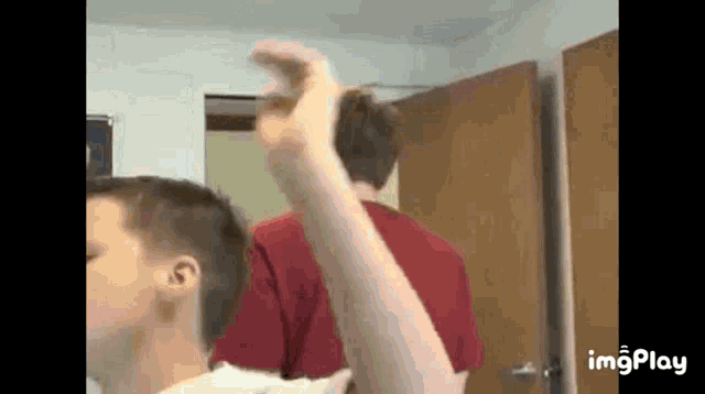 a man is cutting another man 's hair in a room with a door in the background .