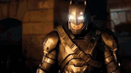 a close up of a person wearing armor and a batman mask standing in a dark room .