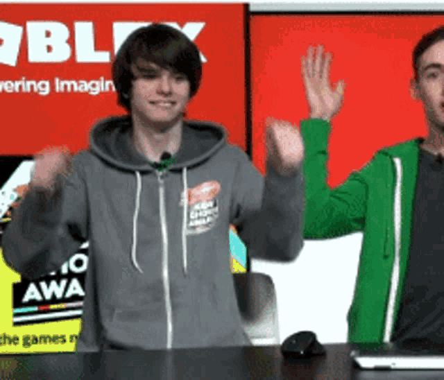 two men are standing in front of a red sign that says roblox