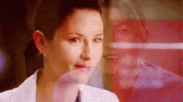 a woman in a lab coat is looking out a window at a man .