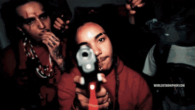 a man holding a gun in front of another man with the words worldstarhiphop.com on the bottom right