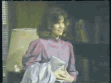 a woman in a purple shirt is standing in front of a lamp holding a bag .