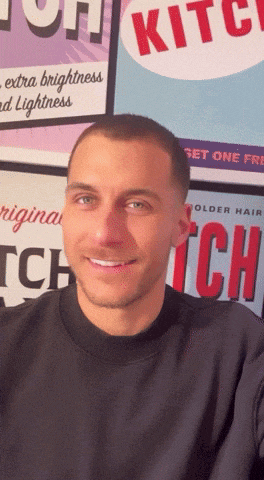 a man is smiling in front of a poster that says kitch