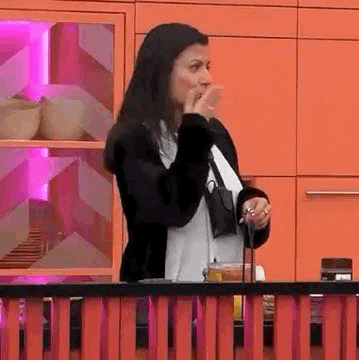 a woman is sitting at a table in a kitchen holding a cup and a microphone .