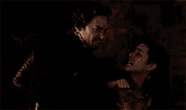 a man is holding a woman who is crying in a dark room