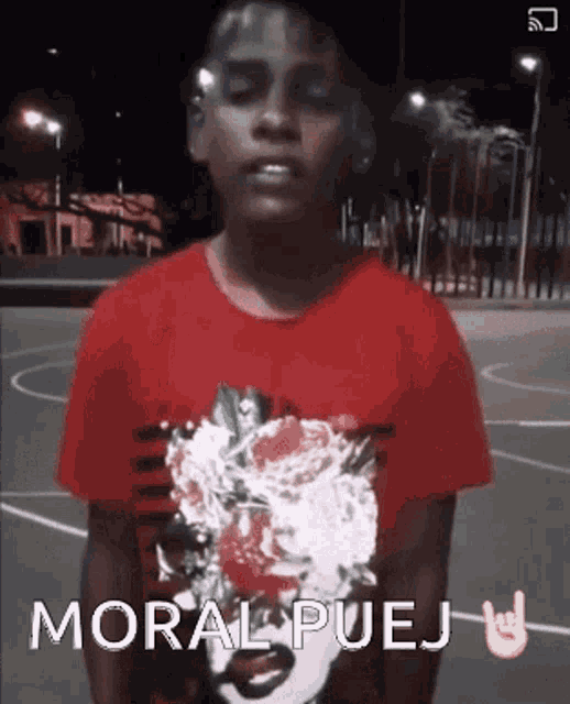a boy wearing a red shirt that says moral puej is standing on a basketball court