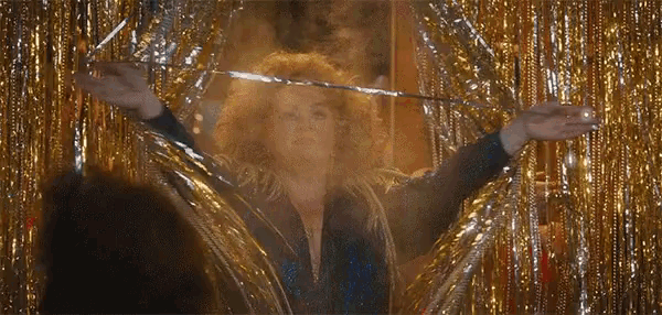 a woman is standing in front of a gold tinsel curtain