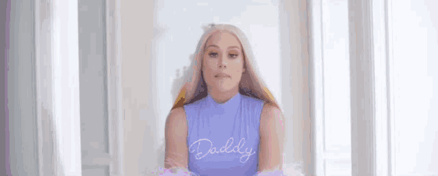 a woman with long blonde hair is wearing a purple top that says daddy .