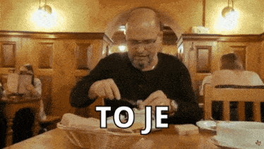 a man sitting at a table with a basket of bread and the word to je written on the table