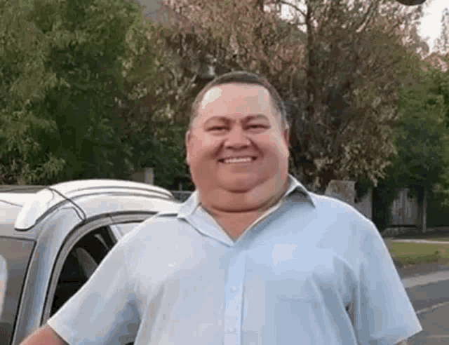 a man in a blue shirt is smiling in front of a car .
