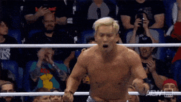 a man without a shirt is standing in a boxing ring with his mouth open .