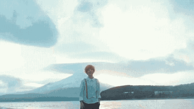 a person is standing in front of a lake with a mountain in the background .