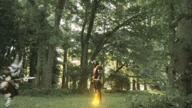 a man in a black and orange costume is walking through a lush green forest