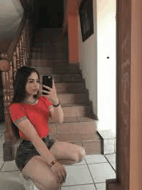 a woman is kneeling down in front of a mirror taking a selfie with her phone .