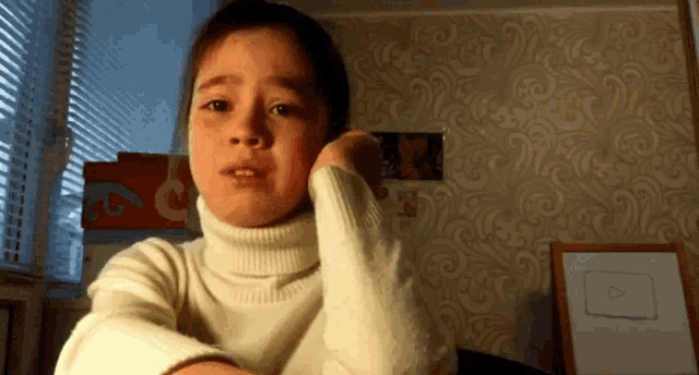 a child in a white turtleneck sweater is looking at the camera