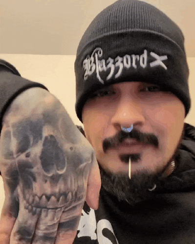 a man with a beard and a tattoo on his hand is wearing a beanie with the word blizzard on it