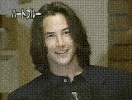 a close up of a man with long hair smiling in a black shirt .