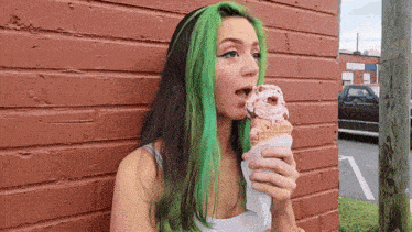 a woman with green hair is eating ice cream in front of a brick wall