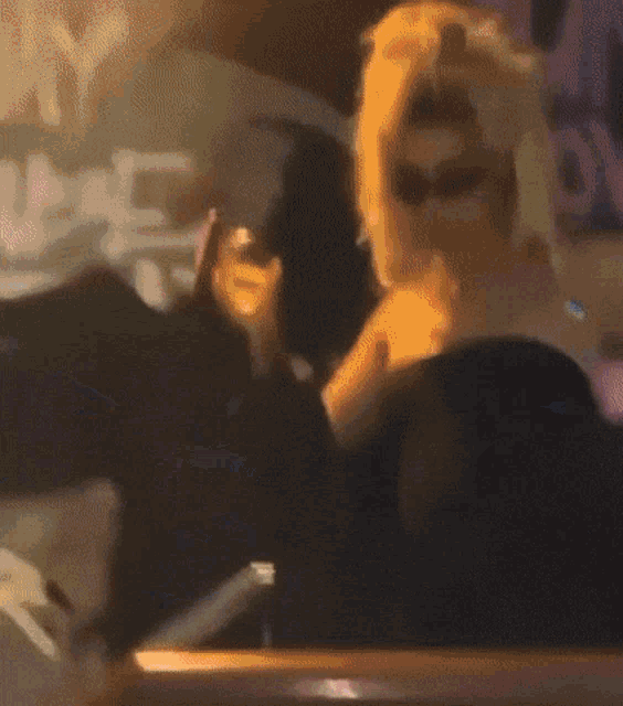 a blurry picture of a woman sitting at a table with a drink in her hand .