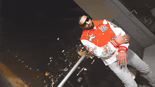 a man wearing sunglasses and a varsity jacket with the letter s on the front