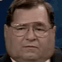 a close up of a man wearing glasses and a suit making a sad face .