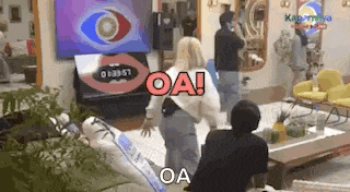 a group of people are standing in a living room with a woman standing in front of a television .