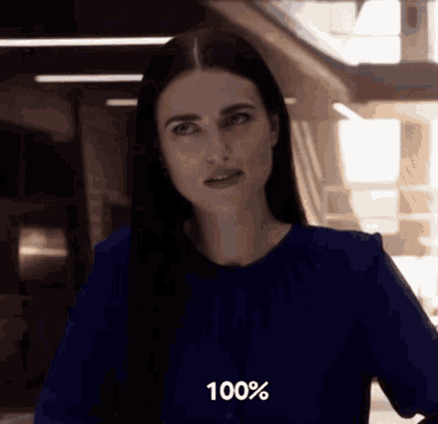 a woman in a blue shirt is standing in a hallway and looking at the camera .