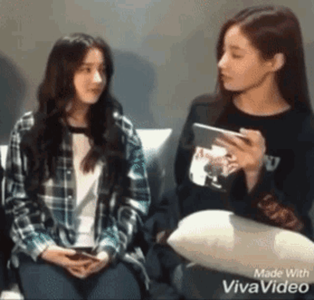 two girls are sitting next to each other on a couch .