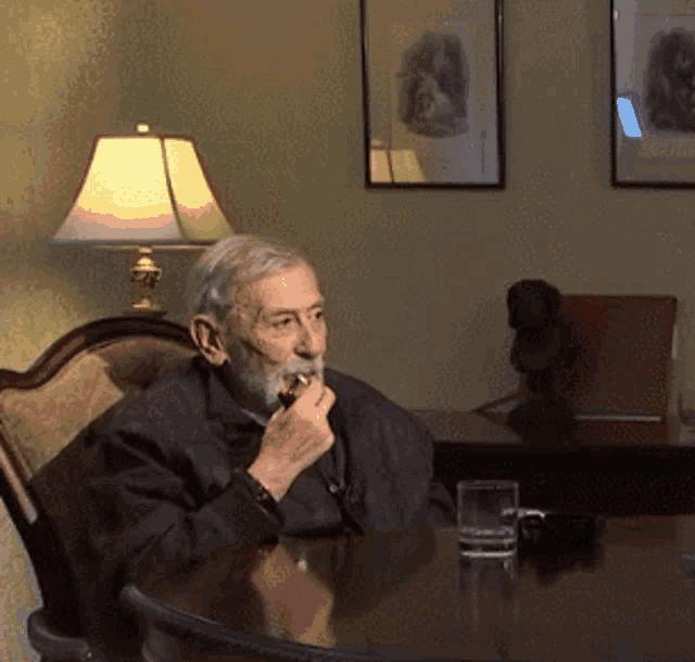 an older man sits at a table with a glass of water