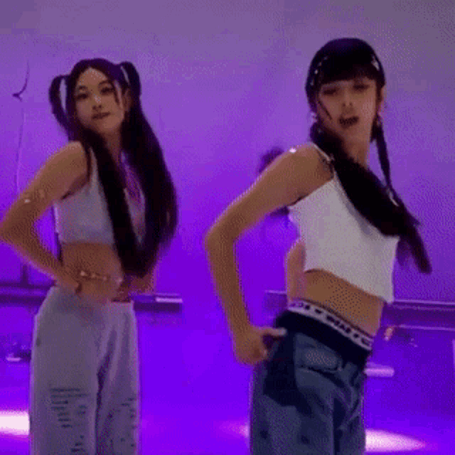 two young girls are dancing together on a stage in a purple room .