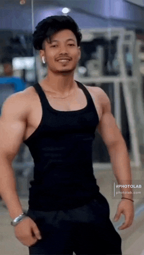 a man in a black tank top is standing in a gym and smiling .