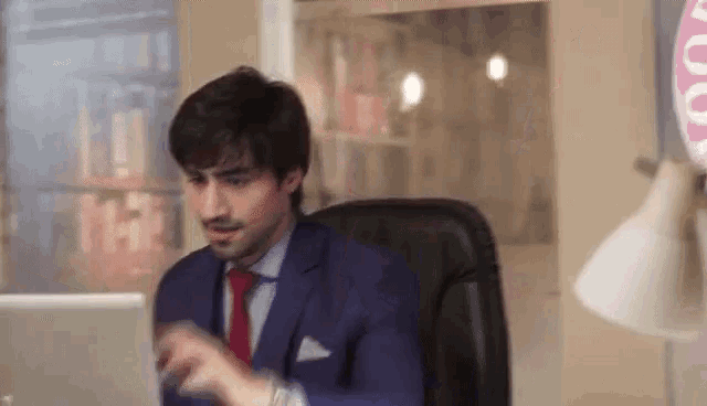 a man in a suit and tie is sitting in front of a laptop computer in an office .